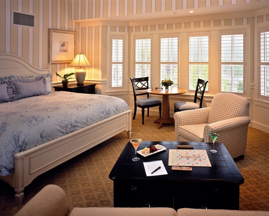 Signature Collection room with a double bed, bedside table with a lamp, a small table with chairs, an armchair, and a coffee table with a Scrabble game, notebook, pen, and two drinks on it.