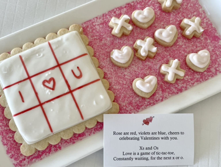 A rectangular plate with frosted cookies. One cookie shows "I ♥ U" in red, while smaller X and O cookies are arranged beside it. A poem with a heart image on paper is also on the plate.