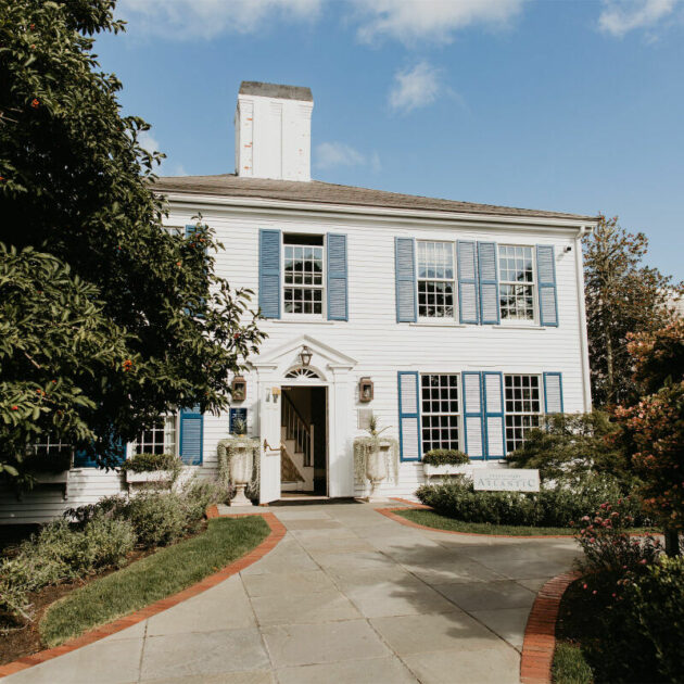 Two-story white building with blue shutters, a central entryway, and a pathway leading to the door.