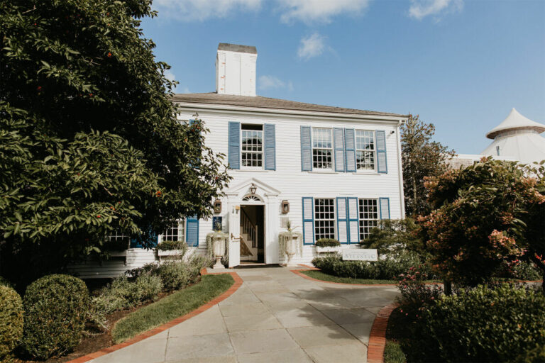 Two-story white building with blue shutters, a central entryway, and a pathway leading to the door.