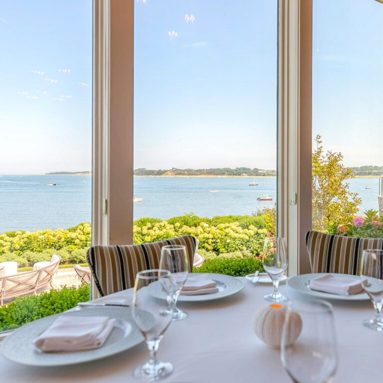 A dining table in front of a large glass window with an ocean view.